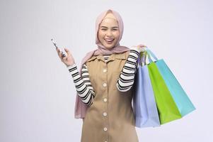 Young beautiful muslim woman in suit holding colorful shopping bags over white background studio photo