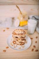 Stack of delicious pancakes with honey, nuts and slices of banana.