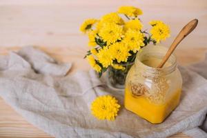 A jar of solid honey and flowers on wooden background.