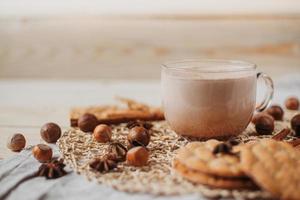 Hot cocoa with cookies, cinnamon sticks, anise, nuts on wooden background. photo