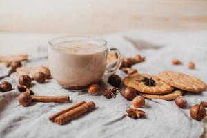 Hot cocoa with cookies, cinnamon sticks, anise, nuts on wooden background. photo