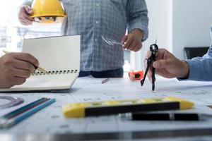 manos de arquitecto o ingeniero usando brújula de dibujo con plano en el escritorio en la oficina. equipo de arquitectos ingenieros discutiendo y verificando documentos y flujo de trabajo empresarial. concepto de construcción. foto