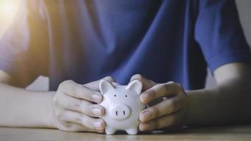 Portrait of teen boy holding and giving white piggy bank in garden. Concept for saving money, loan, property ladder, financial, real estate investment and bonus. photo