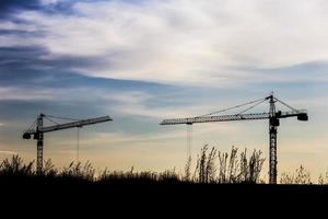 Industrial construction cranes and building silhouettes over sun at sunrise
