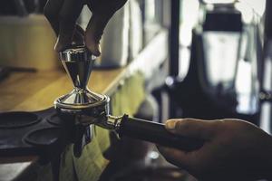 el barista está usando su mano para presionar el café en polvo en el bloque en caso de que el café recién tostado se extraiga de la máquina de transmisión. foto