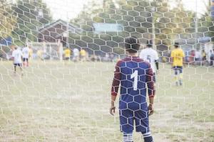 Goalkeeper stands against goal with net and stadium. Football gate net. Behind goal of soccer field.