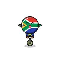 el lindo personaje de la bandera de sudáfrica está montando una bicicleta de circo vector