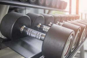 Black dumbbell set. Close up many metal dumbbells on a rack in the sports fitness center. photo