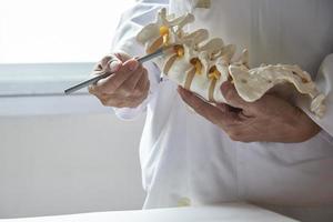 un médico señalando el modelo de vértebra lumbar en el consultorio médico