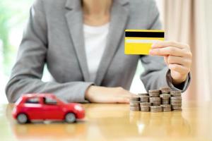 tarjeta de crédito de asimiento de la mano de la mujer de negocios, un coche de juguete y una pila de monedas foto