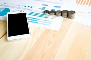 Stack coin and smartphone on table with statistic graph diagram photo