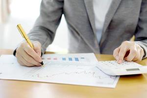 Close-up Of Businesswoman Analyzing Financial Report With Calculator At Wooden photo