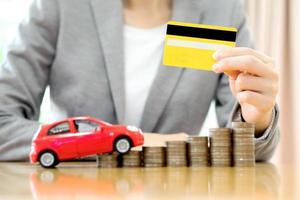 tarjeta de crédito de asimiento de la mano de la mujer de negocios, un coche de juguete y una pila de monedas foto