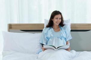 mujer embarazada en el dormitorio leyendo cuentos de hadas al bebé en el útero por la mañana foto
