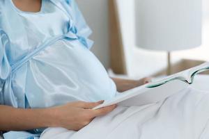Pregnant woman in bedroom reading fairy tales to the baby in the womb in the morning photo