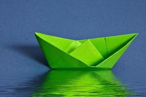 Green paper boat near  water with reflection