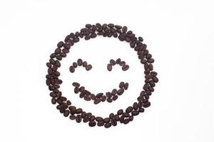 granos de café tostados dispuestos en una cara sonriente sobre un fondo blanco. foto