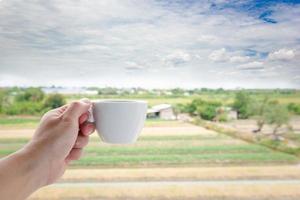 A white man's hand holding a hot coffee mug on the landscape field nature background. photo