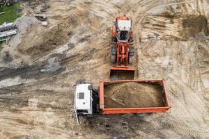 an excavator loads sand into a truck on a construction site. Top view from a drone. photo