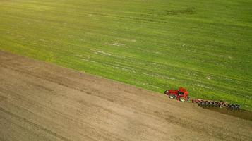 Agricultural tractor rides across the field with a seed drill spreading mineral fertilizers photo