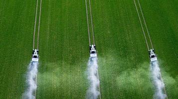 tres tractores rocían pesticidas en una vista superior del campo verde foto