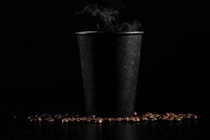 A black glass of hot coffee with scattered coffee beans on a black background. close-up photo