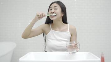 jovem mulher limpando os dentes com uma escova de dentes no banheiro em frente ao espelho admirando seu reflexo