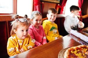 Children on birthdays sitting at the table and eating pizza. photo