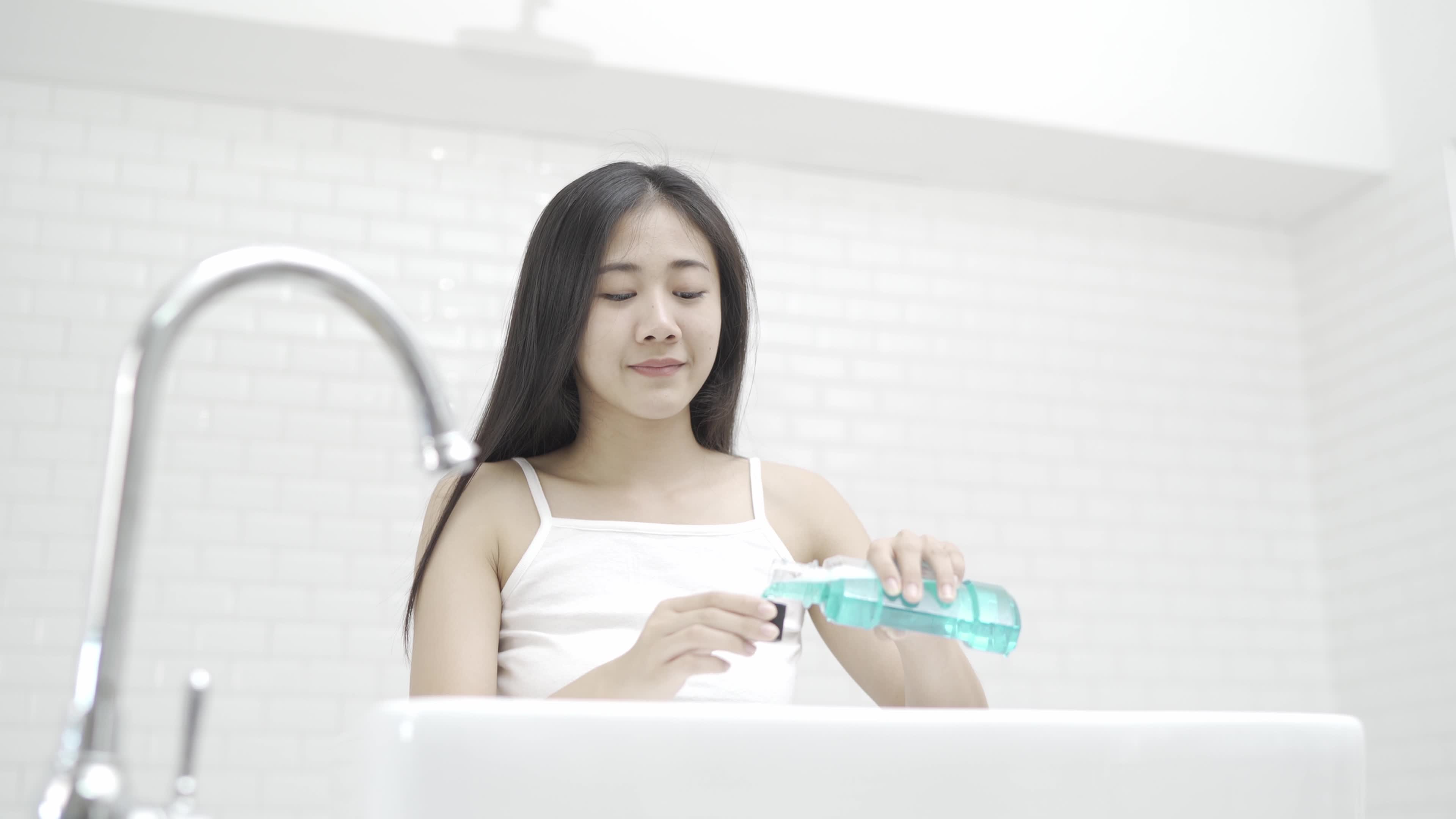 A cute Asian woman brushing her teeth and gargling in front of the mirror after waking up every morning.