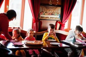 Children on birthdays sitting at the table and eating pizza. photo