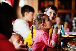 niños en cumpleaños sentados en la mesa y comiendo pizza. chica bebe jugo. foto