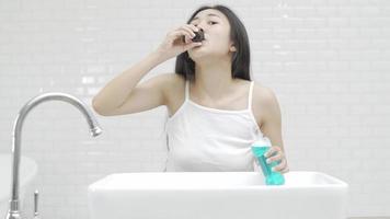una linda mujer asiática cepillándose los dientes y haciendo gárgaras frente al espejo después de despertarse cada mañana.