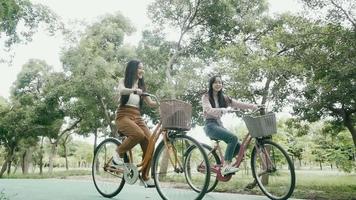 des dames souriantes sur les deux vélos pour filles roulent dans le parc au printemps. video