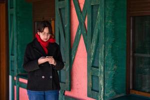 a girl with a phone in her hands stands on the street near a pink house with green shutters photo