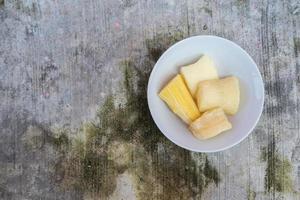 Boiled cassava is better than fried cassava, cassava in white bowl with shadow of leaves, isolated on concrete floor photo