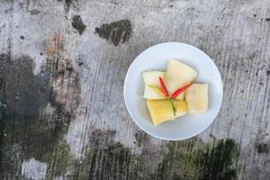 Boiled cassava is better than fried cassava, cassava in white bowl with shadow of leaves, isolated on concrete floor photo