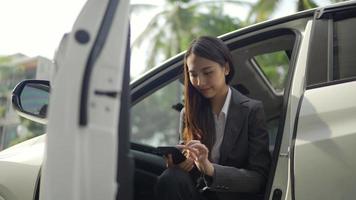 Beautiful young Asian woman in casual clothing talking by mobile phone and smiling in sitting back seat of car in urban modern city.