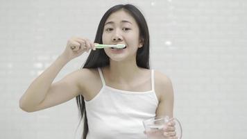 mujer joven limpiándose los dientes con un cepillo de dientes en el baño parada frente al espejo admirando su reflejo video