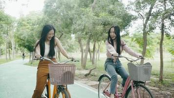 des dames souriantes sur les deux vélos pour filles roulent dans le parc au printemps. video