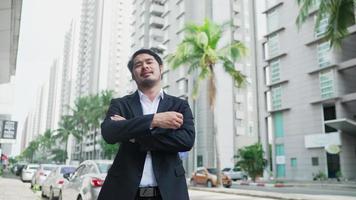 retrato feliz amistoso hombre de negocios asiático de pie en el fondo de la calle de la ciudad urbana fuera. oficinista de hombre de negocios en traje formal cerca del edificio de oficinas moderno mirando a la cámara sonriendo video