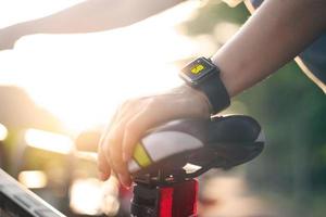 mujer ciclista mano con reloj inteligente en bicicleta de silla de montar en sendero de verano. foto