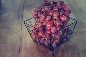 Bunch of red grape in metal basket on wooden table background photo