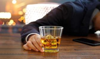 hombre de negocios con whisky bourbon en la mano, borracho durmiendo en la mesa del pub foto