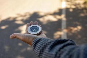 Male traveler holding a magnetic compass on asphalt road, orientation and finding your way. photo