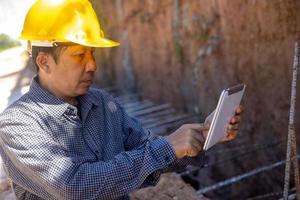 architect or civil engineer with hardhat on construction site checking schedule on tablet computer photo