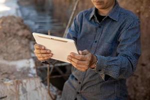 architect or civil engineer with hardhat on construction site checking schedule on tablet computer photo