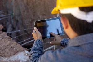 architect or civil engineer with hardhat on construction site checking schedule on tablet computer photo