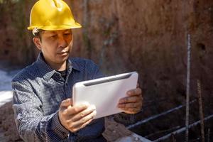 architect or civil engineer with hardhat on construction site checking schedule on tablet computer photo