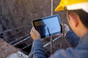 architect or civil engineer with hardhat on construction site checking schedule on tablet computer photo