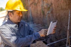 architect or civil engineer with hardhat on construction site checking schedule on tablet computer photo